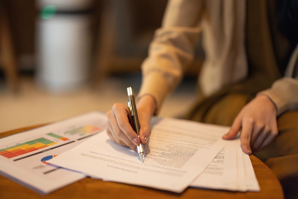 A woman is sitting at a table writing on a piece of paper with a pen.