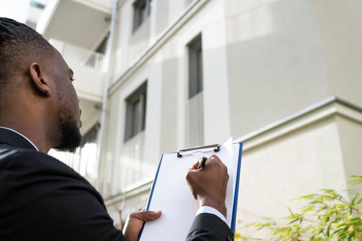 A man is writing on a clipboard in front of a building.