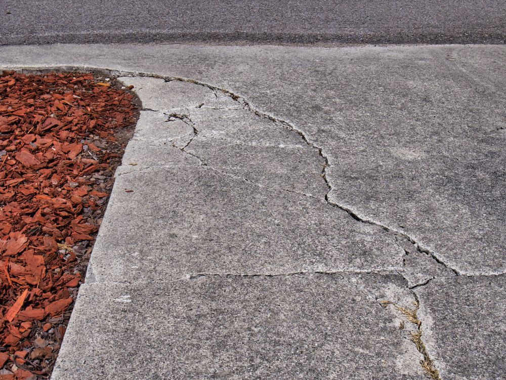 A close up of a cracked concrete sidewalk next to a road.