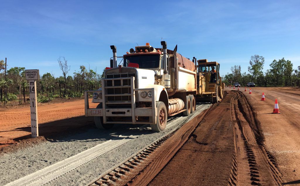 A Truck Is Driving Down A Dirt Road Next To A Bulldozer — Coleman's Contracting & Earthmoving In Humpty Doo, NT
