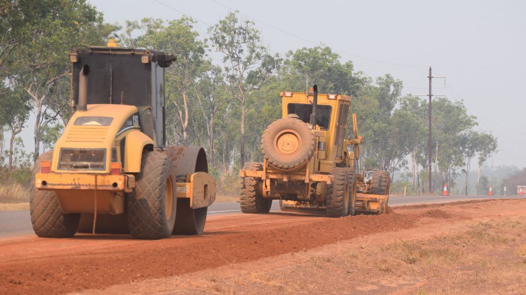 A Yellow Tractor Is Driving Down A Dirt Road — Coleman's Contracting & Earthmoving In Humpty Doo, NT