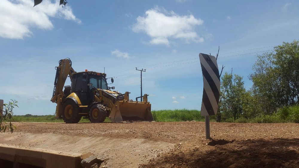A Bulldozer Is Driving Down A Dirt Road Next To A Sign — Coleman's Contracting & Earthmoving In Humpty Doo, NT