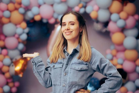 Event planner smiling in front of a balloon arch and birthday number balloons