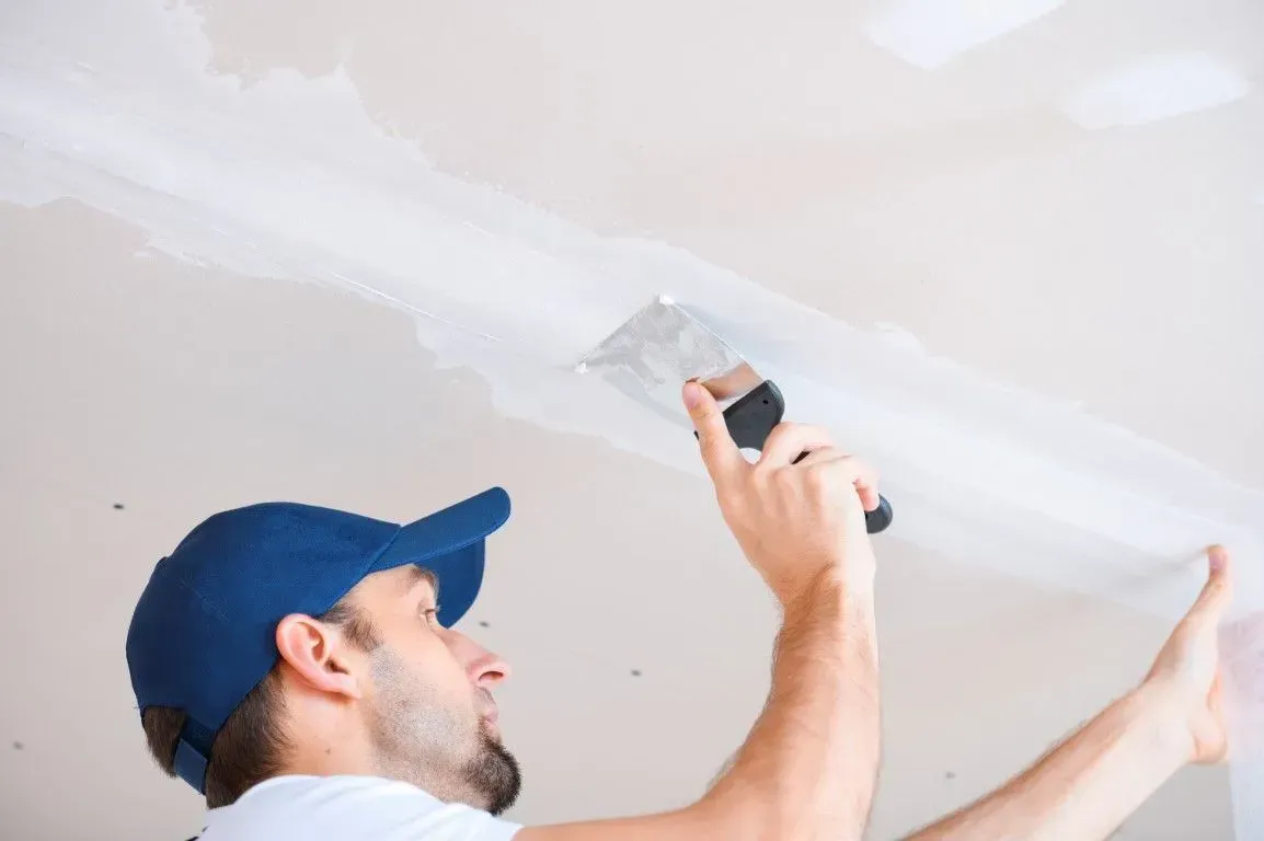 Close-up of worker taping and mudding drywall seams.