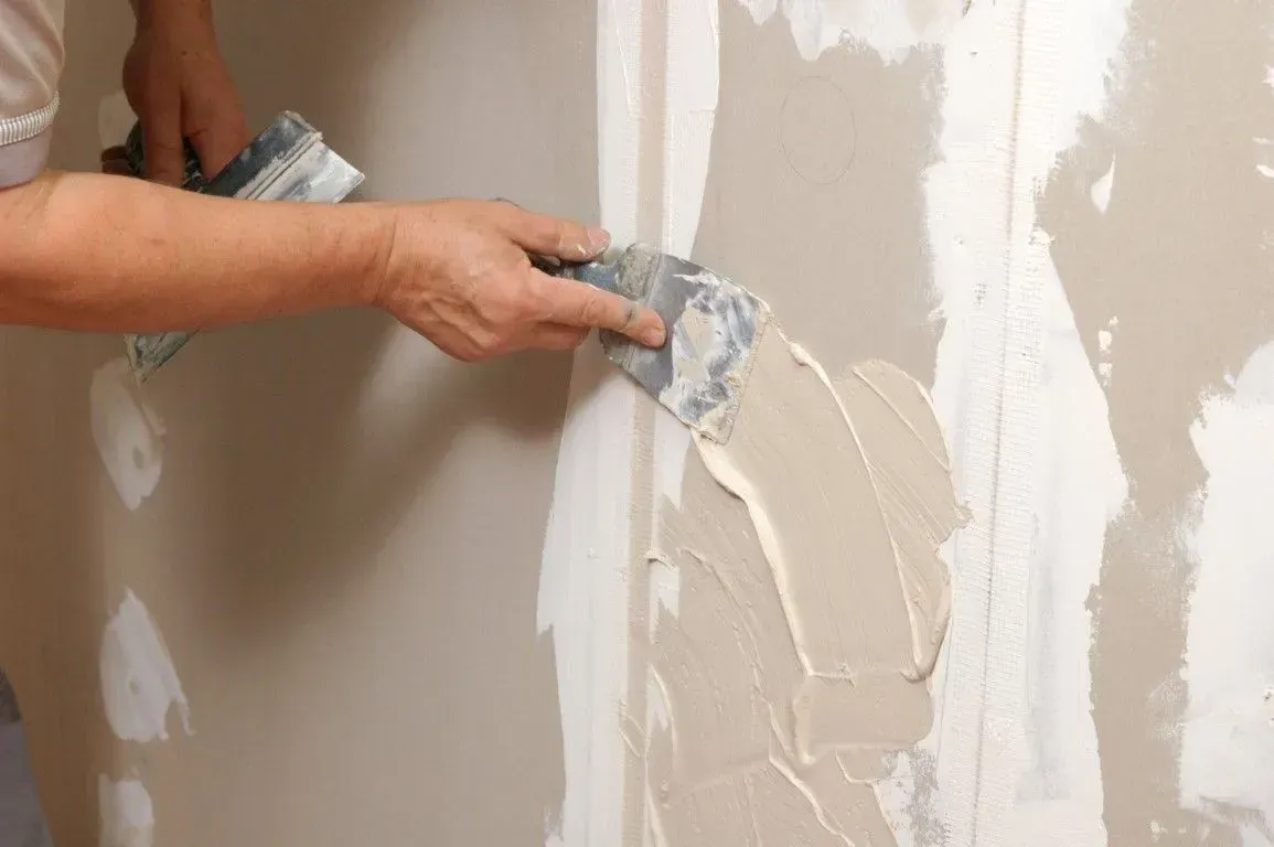 Hand using a putty knife to repair a hole in a drywall.