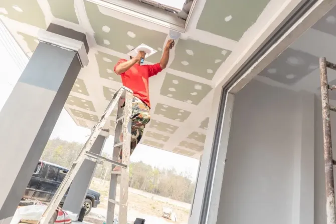 Contractor on a ladder finishing an outdoor porch ceiling.