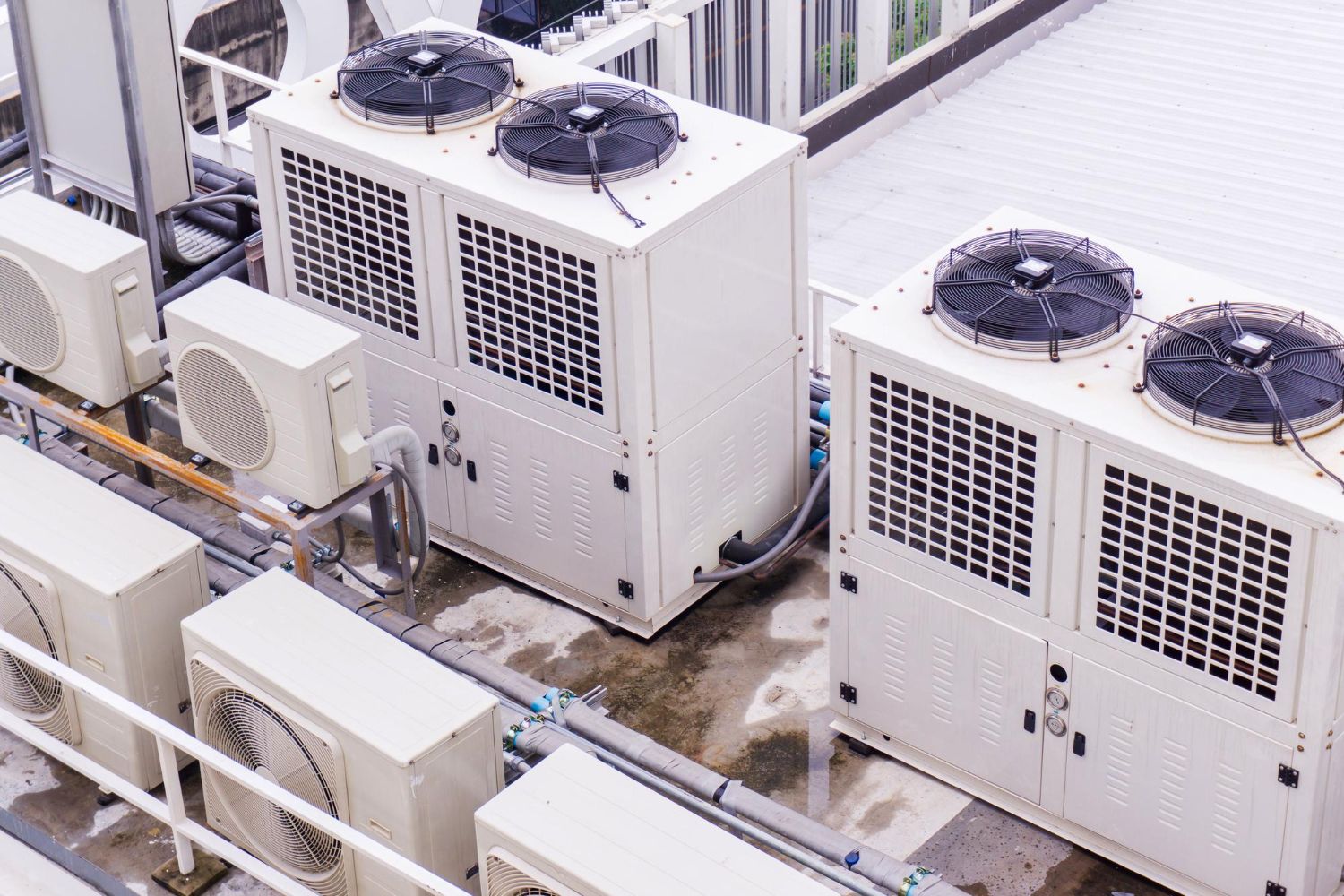Air conditioning units on a rooftop; white and gray, some with fans.