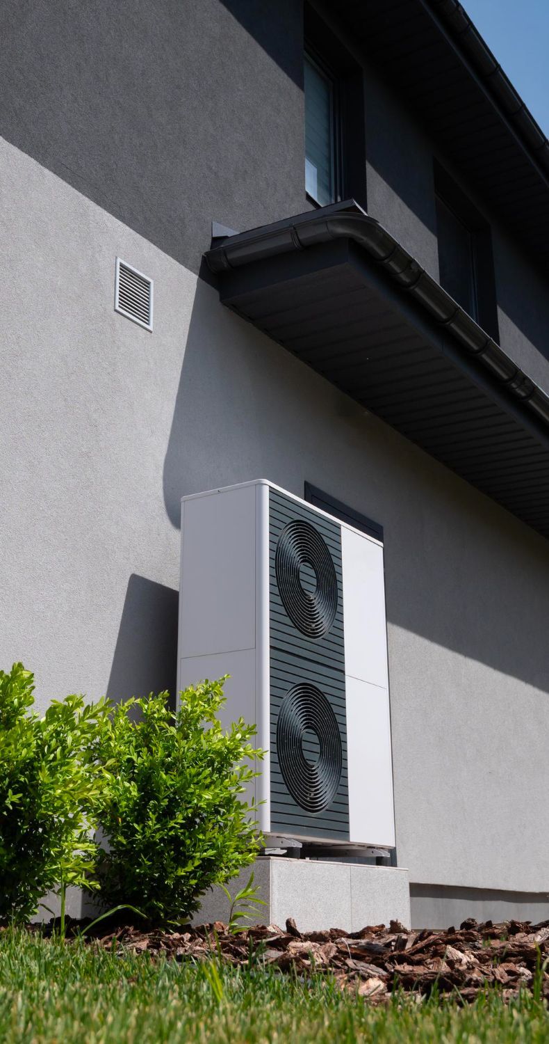 White heat pump unit mounted on exterior wall of a house.
