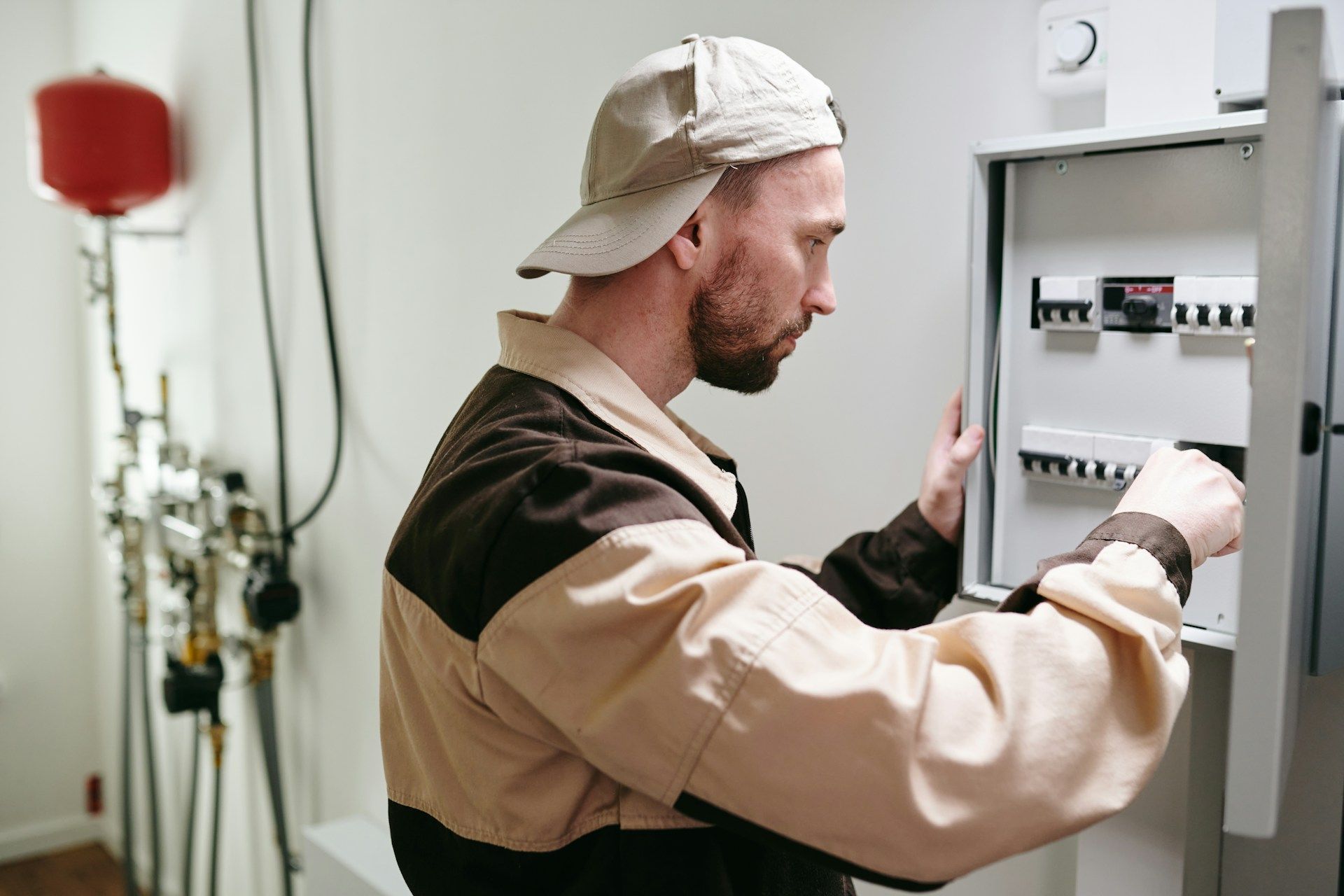 Man in work clothes working on an electrical panel. He’s wearing a cap and appears focused in an indoor setting.
