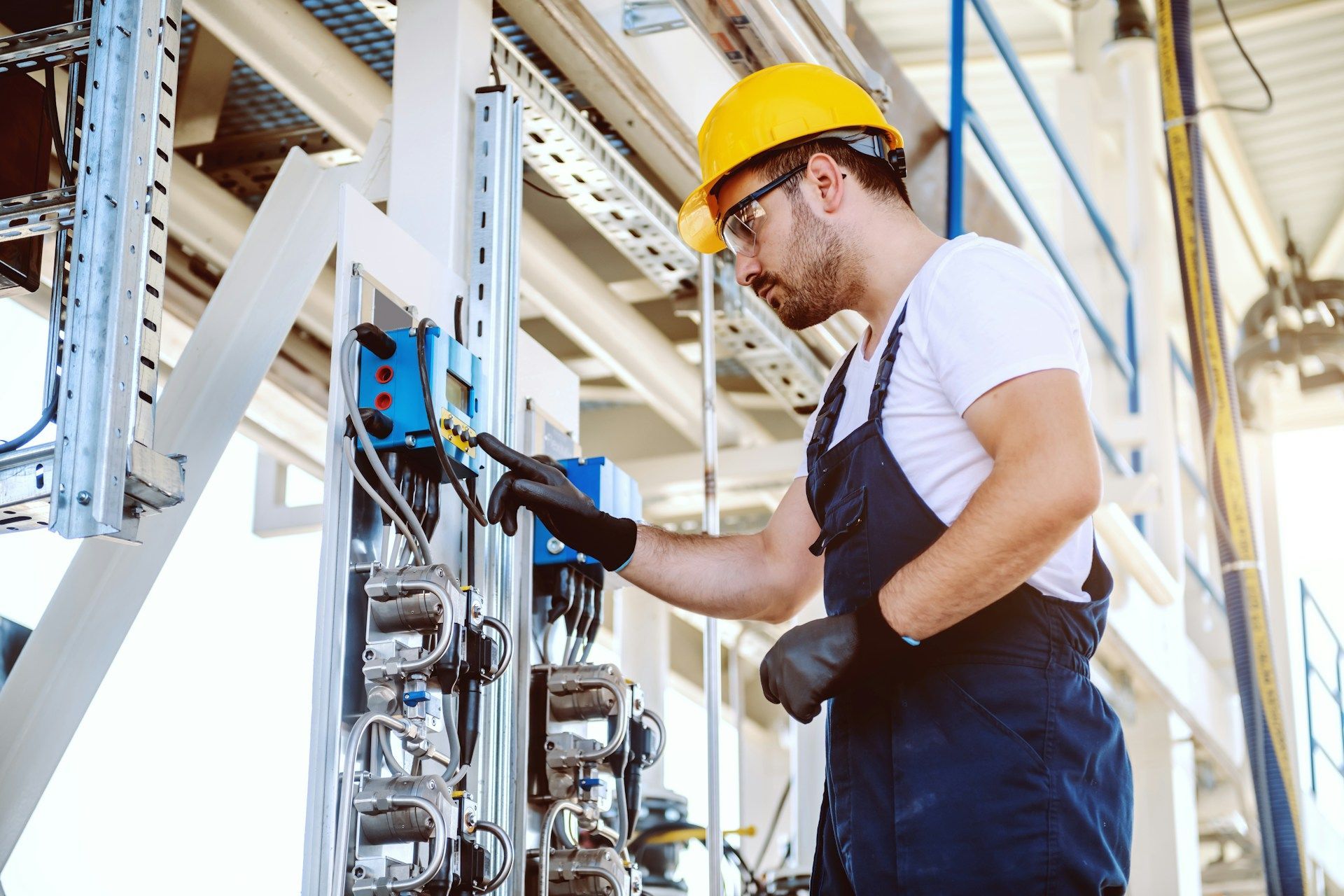 A person in a yellow hard hat and coveralls inspecting electrical equipment.