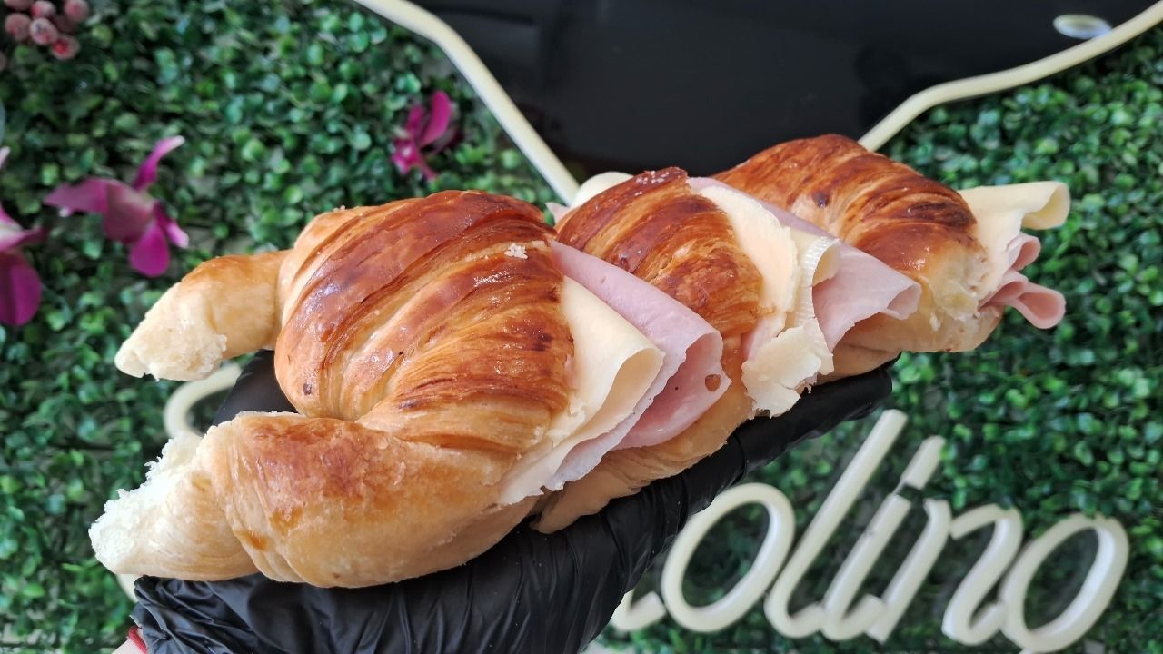 Una persona sostiene un croissant con jamón y queso encima.