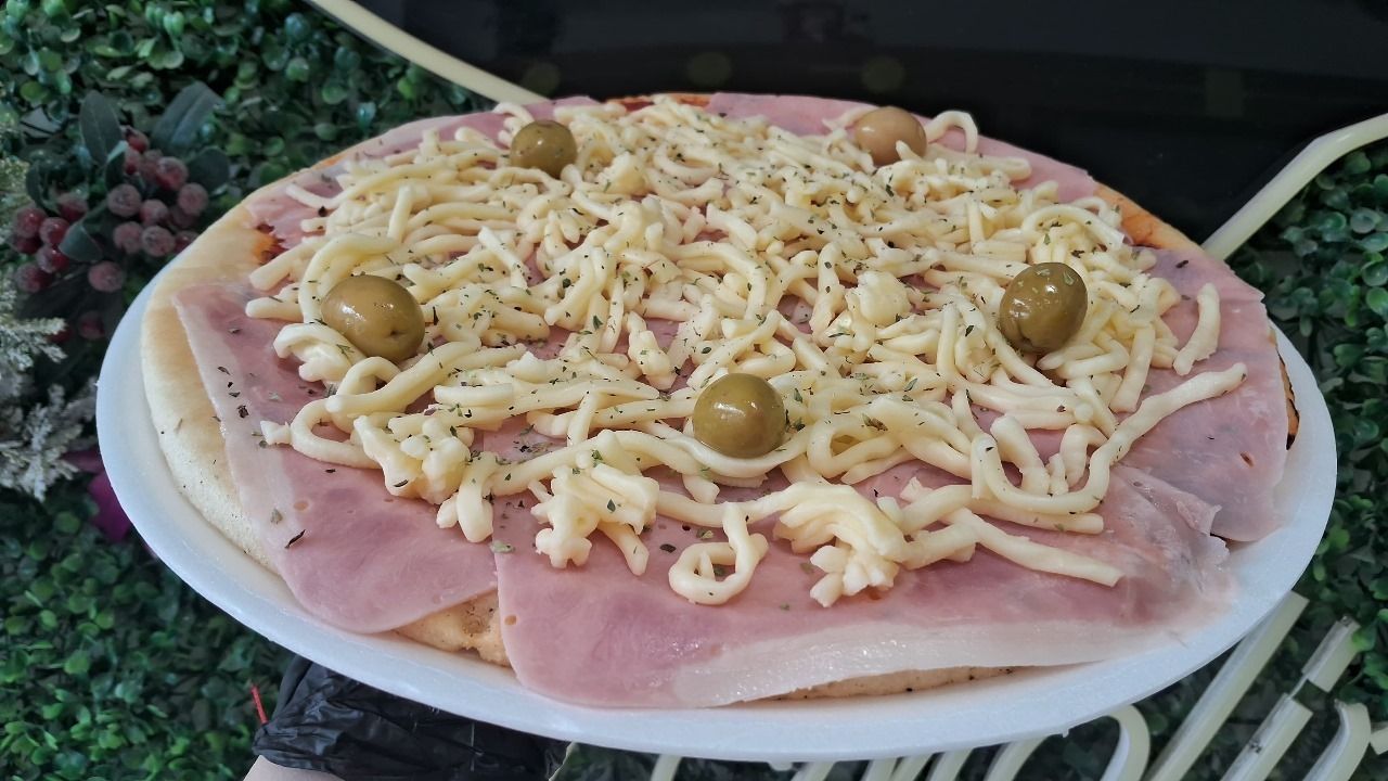 Una pizza con jamón, queso y aceitunas en un plato blanco.
