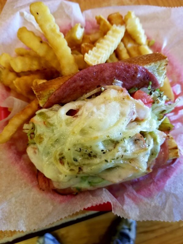 A hot sandwich topped with melted cheese and cured meat, served with a side of crinkle-cut fries in a paper-lined basket.