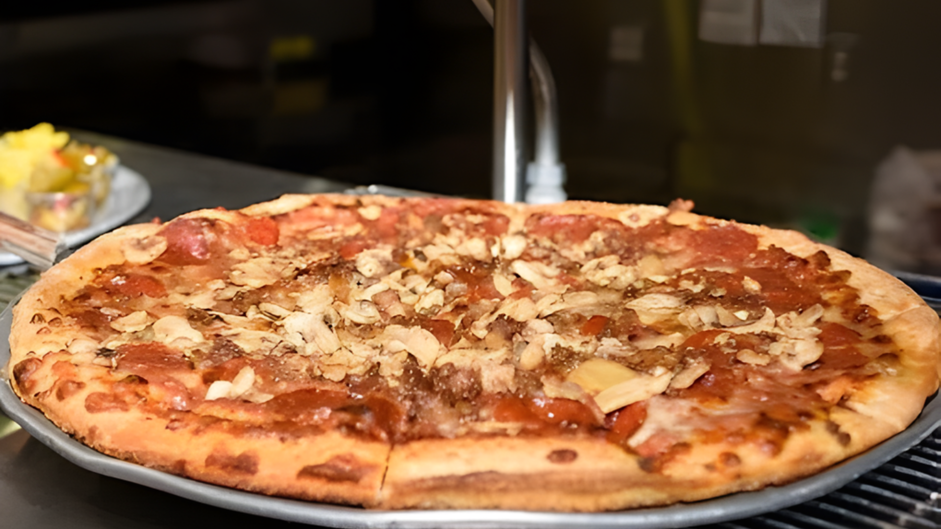 A pepperoni pizza topped with sliced mushrooms sits on a metal tray in a kitchen setting.