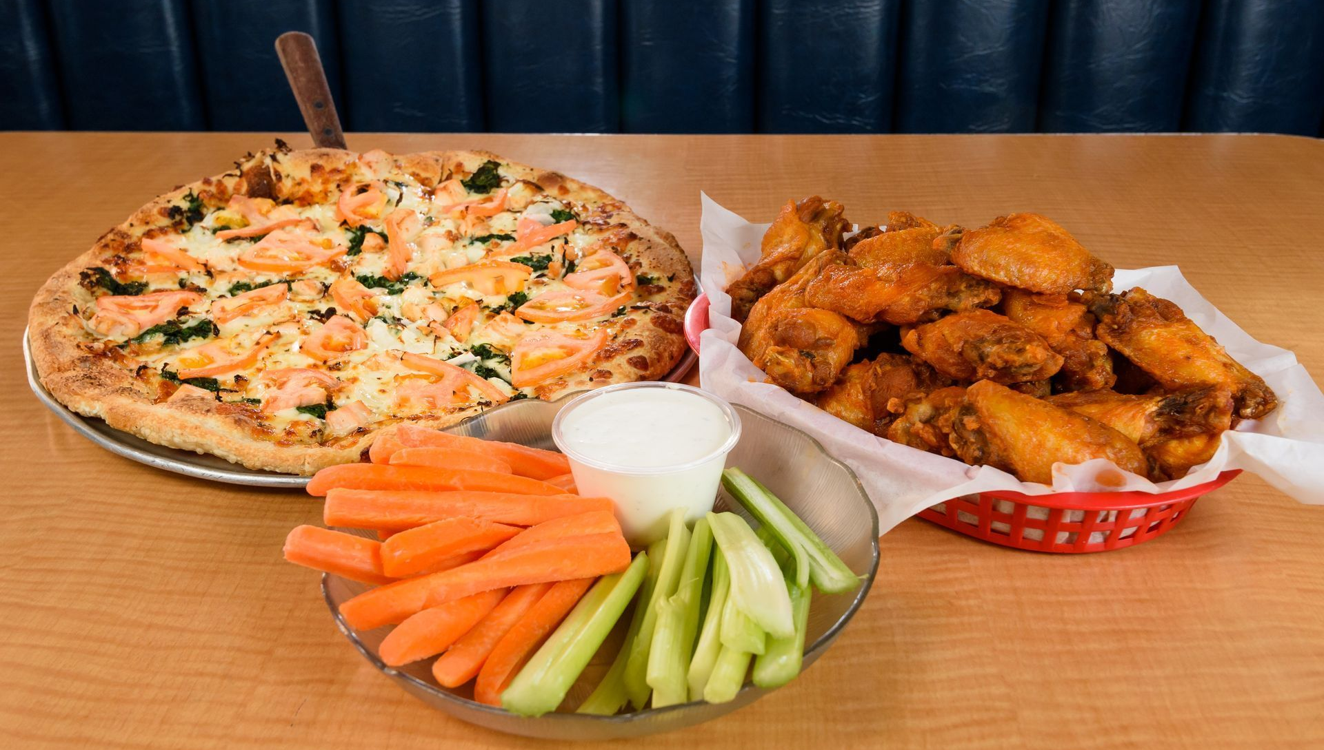 Pizza, chicken wings, and veggie sticks with dip on a wooden table