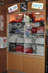 A glass display case filled with folded shirts and hats, topped with two license plates reading UNC SAM and AUNTSAM.