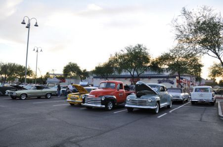 A car show in a parking lot featuring several classic vintage vehicles, including an orange truck and silver sedans.