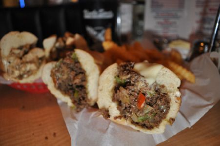 A close-up of two halves of a cheesesteak sandwich filled with meat, peppers, and onions, served on parchment paper.