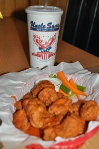A basket of buffalo-style chicken wings with celery and carrots next to an 