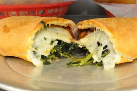 A golden-brown spinach and melted cheese calzone sliced open on a metal plate, with a red plastic basket in the background.