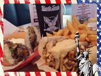 A Philly cheesesteak sandwich and a basket of fries next to an Uncle Sam's cup, framed by an American flag border.