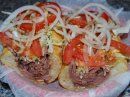 Two sandwiches on a platter topped with fresh tomato slices and thin, raw white onion strips.