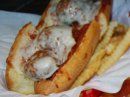 A meatball sub sandwich covered in melted cheese, served with a side of french fries on a white paper liner.