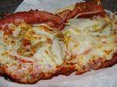 An open-faced, toasted sandwich or sub, topped with melted white cheese and visible savory fillings on a white wrapper.