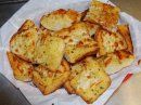 A basket filled with golden-brown, toasted pieces of garlic bread topped with melted cheese and herbs.