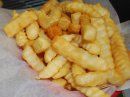 A close-up of a basket lined with white paper filled with golden-brown crinkle-cut french fries.