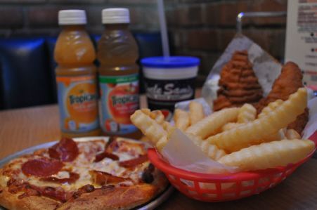 A pepperoni pizza, crinkle-cut fries in a red basket, and two Tropicana bottles on a restaurant table.