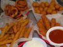 Four baskets of golden-brown fried appetizers, including onion rings, breaded nuggets, fries, and mozzarella sticks.