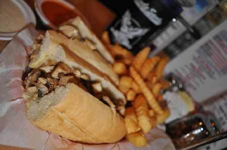 A mushroom sandwich served in a basket with a side of crinkle-cut fries on a table with condiments.