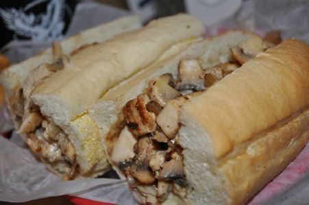 Two long sub sandwiches filled with grilled chicken and mushrooms resting on a white wrapper in a red basket.