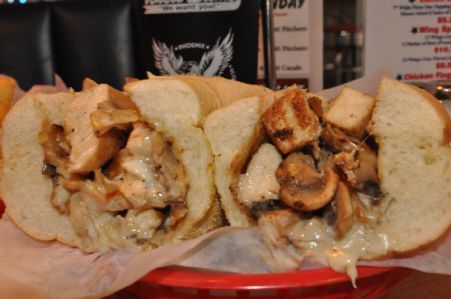 Two halves of a chicken and mushroom cheesesteak sub, served on white parchment paper inside a red basket.