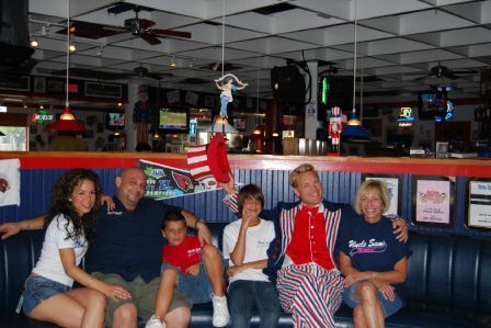 A group of six people sit in a booth at a restaurant, including one person dressed in a red, white, and blue suit.