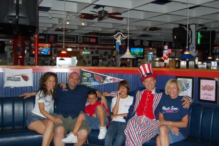 A group of six people sits on a blue booth in a restaurant, one dressed as Uncle Sam, posing for a photo.
