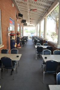 An outdoor covered patio at a restaurant featuring rows of tables with black chairs and two Uncle Sam statues by the wall.