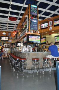 A bar with a stone counter, high stools, and multiple televisions mounted above the service area.