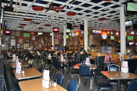 Interior of a sports bar with a white grid ceiling, numerous TVs, and tables with blue chairs arranged throughout.