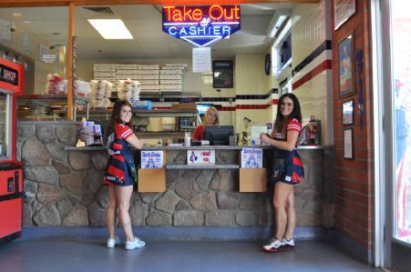 Two people in uniforms standing at a restaurant service counter beneath a glowing 