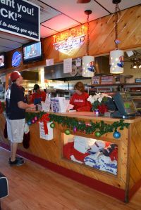 Employees stand behind a wooden counter decorated with holiday garlands at a restaurant service window.