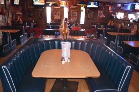 A restaurant interior with blue vinyl booths, wooden tables, and televisions on brick walls.