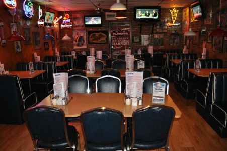 An empty dining room in a restaurant with tables, dark chairs, red brick walls, and hanging neon signs.