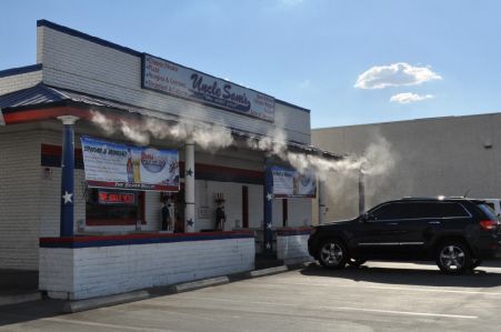 Uncle Sam’s restaurant exterior on a sunny day with a misting system active and a black SUV parked in the lot.
