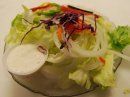 A small bowl of mixed green salad with shredded red cabbage, onions, and a side of white dressing.