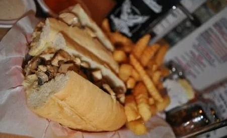 Sandwich and fries on a table, with dipping sauces and a drink in the background.