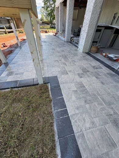 A paved walkway made of light-gray stone tiles with a dark-gray border leads to a building with stone pillars.