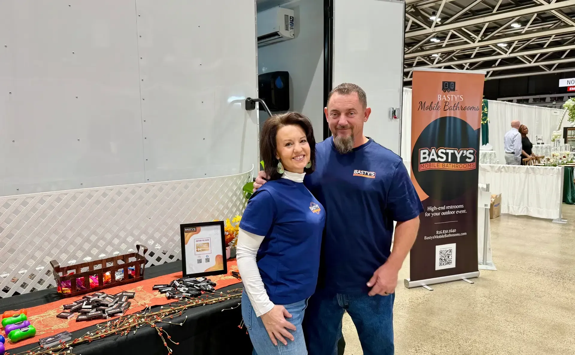 A man and woman stand beside a table at a trade show, engaging with attendees and showcasing products