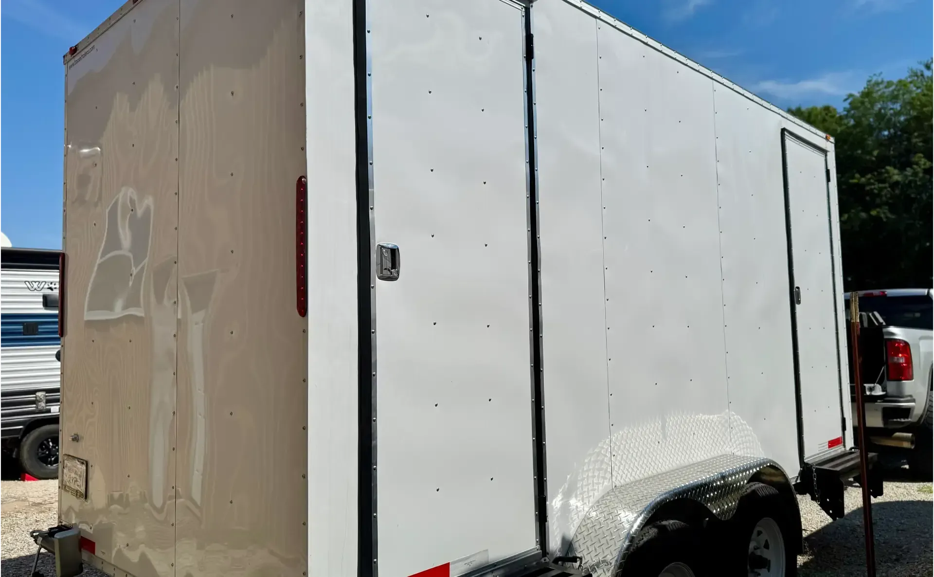 A white enclosed trailer featuring a side door, parked on a flat surface